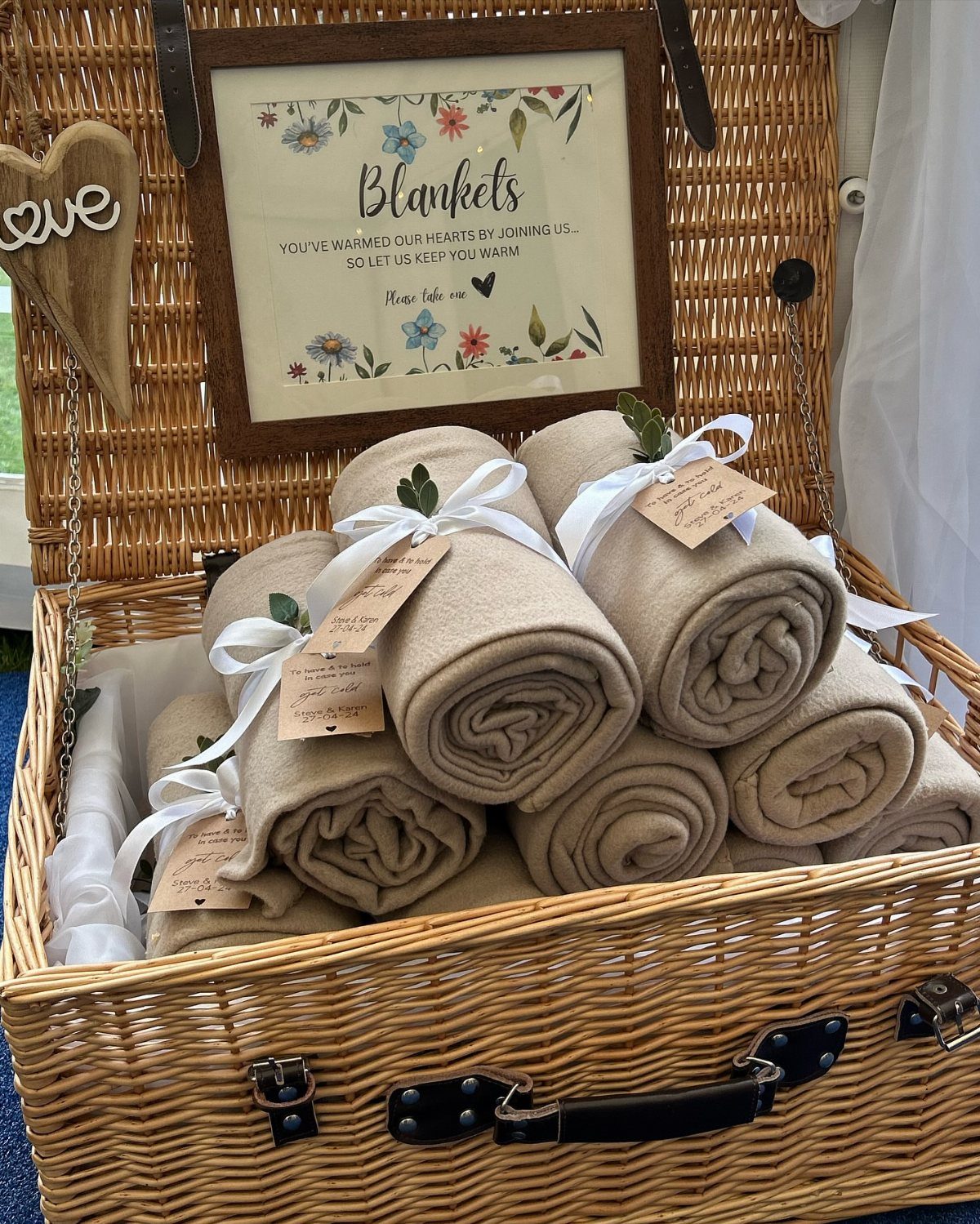Rolled beige throw blankets with white ribbons in a wicker basket with sign.