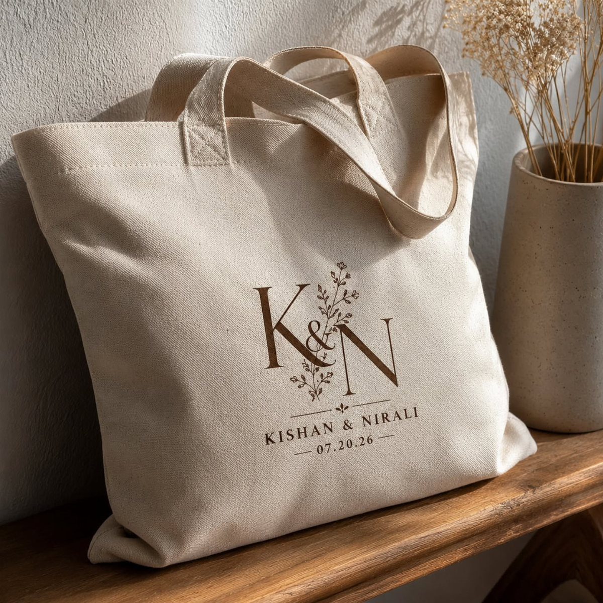 Beige canvas tote bag with personalized wedding initials and names on wooden surface