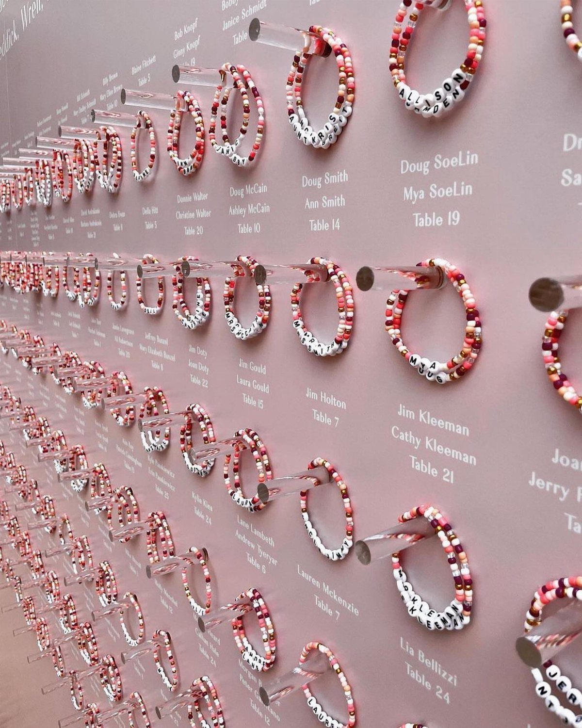 Beaded bracelets hanging on a pink wall with guest names and table numbers.