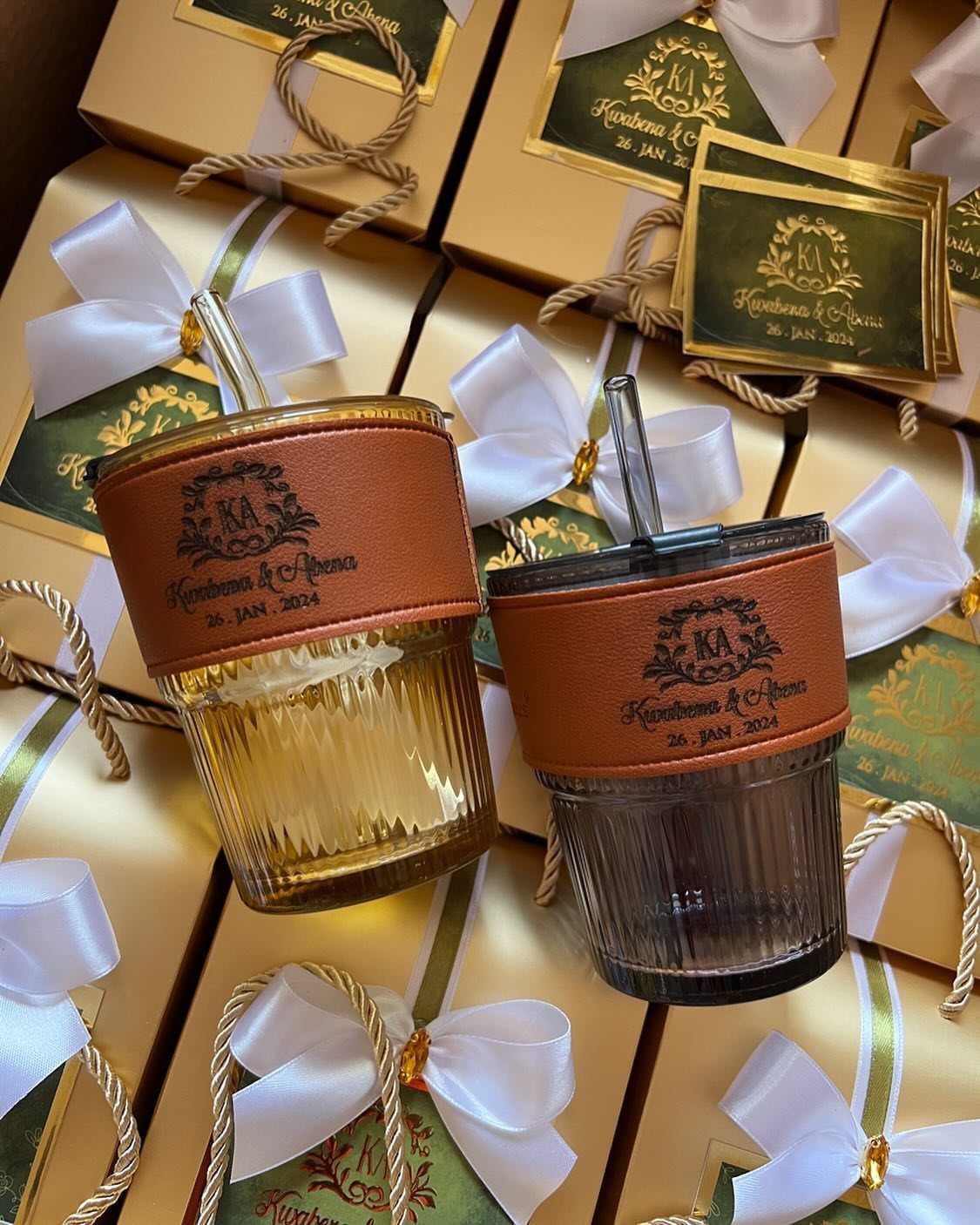 Two personalized ribbed glass tumblers with brown leather sleeves on gift boxes.