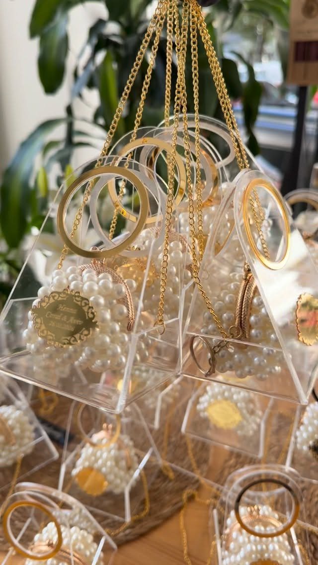 Clear acrylic pyramid boxes containing pearl necklaces with gold charms hanging by chains.