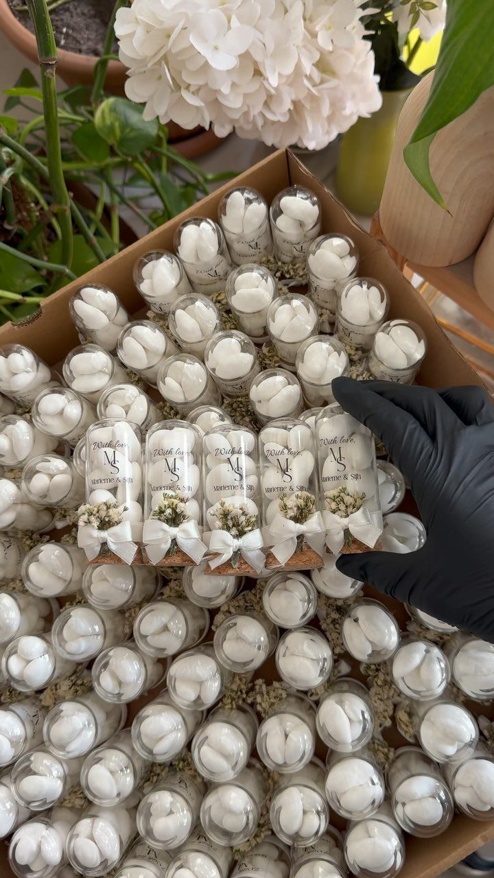 Small glass tubes with white treats and bows arranged in a cardboard box.