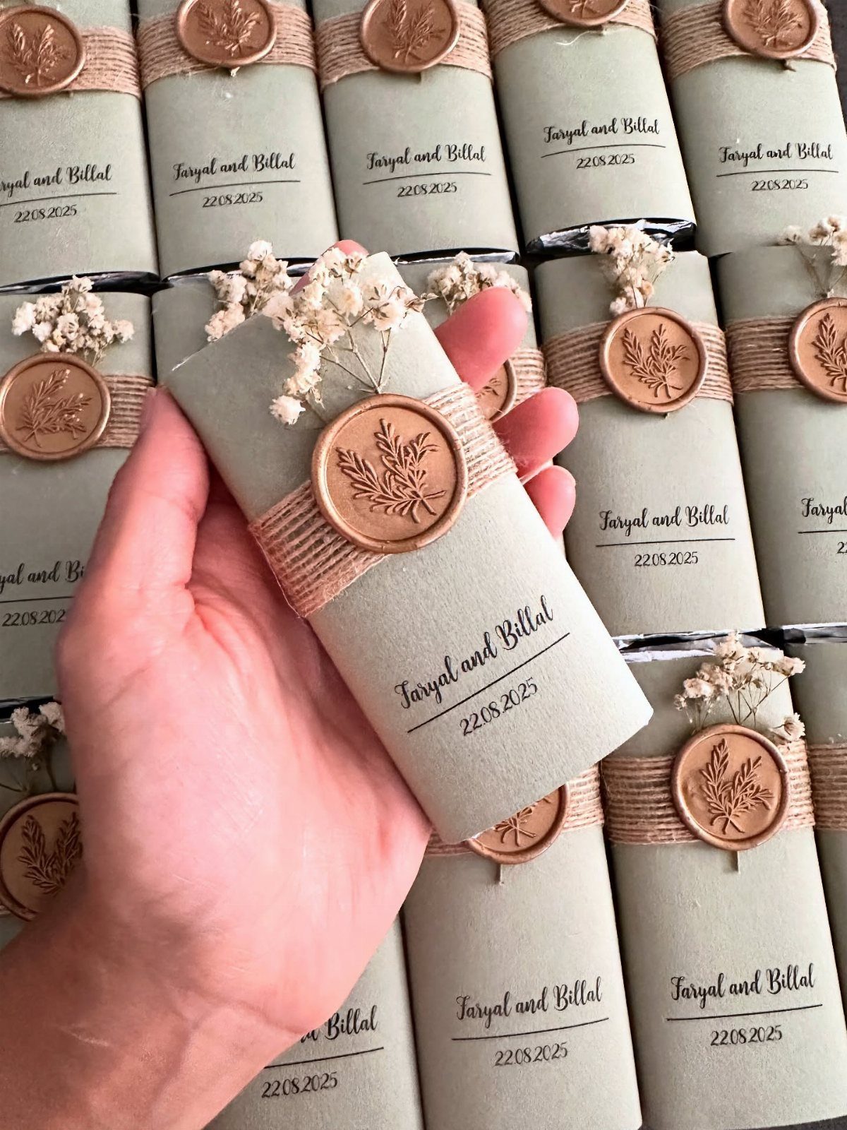 Wrapped cylindrical wedding favors with grey paper, twine, copper wax seals, and dried flowers.