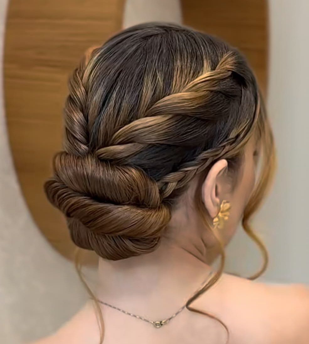 Low bun updo with intricate braids and blonde highlights on brown hair.
