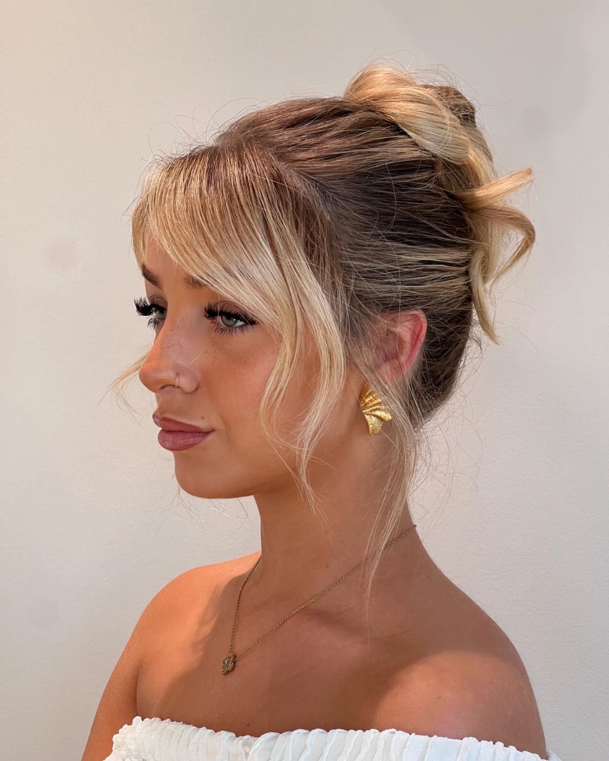 Woman with blonde hair styled in a loose messy bun and bangs
