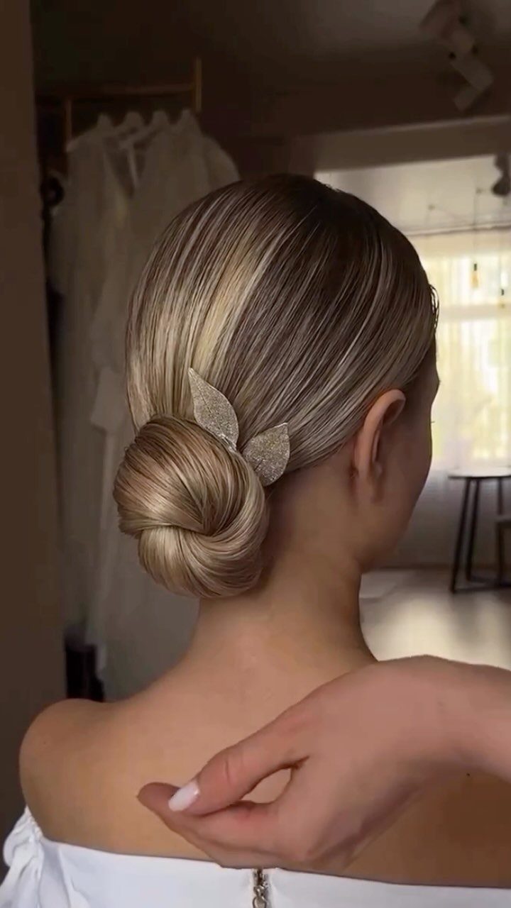 Blonde hair styled in a sleek low bun with a silver leaf accessory
