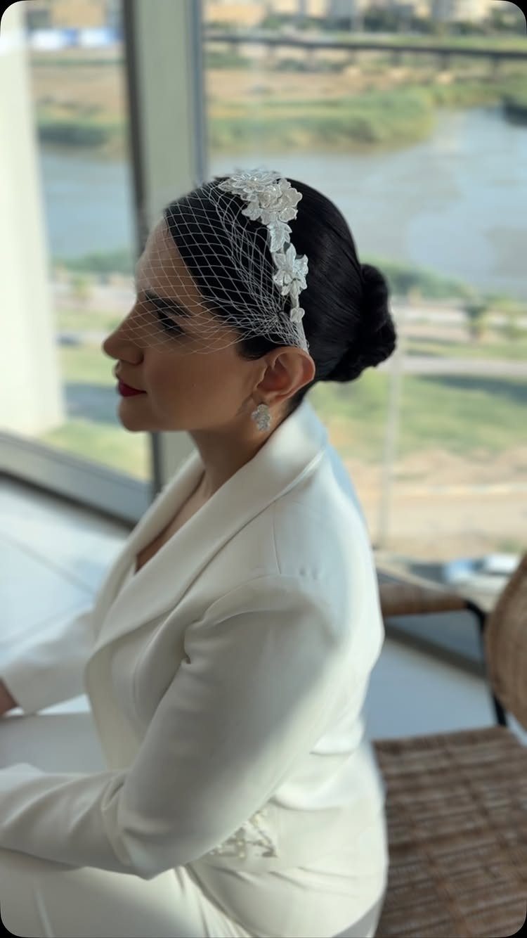 Woman in white suit with low bun and floral birdcage veil