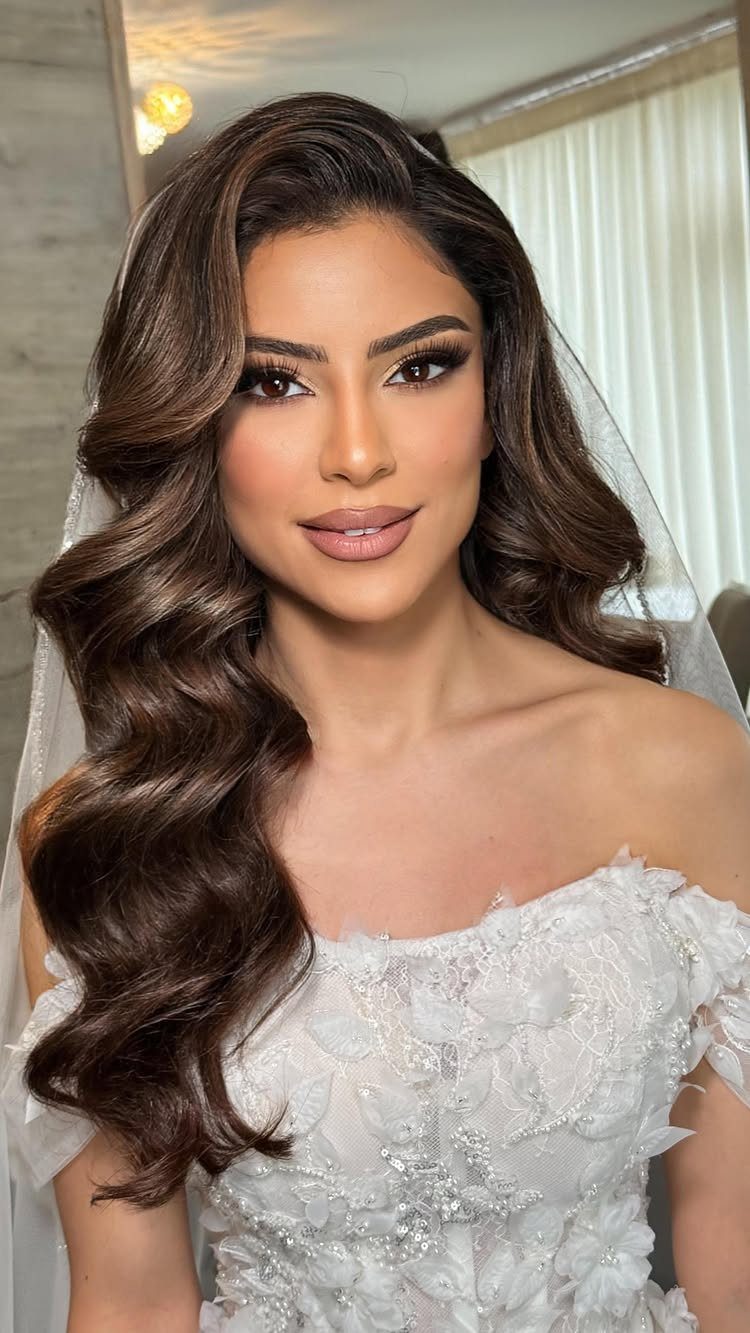 Woman with wavy brown hair wearing a white wedding dress and sheer veil.