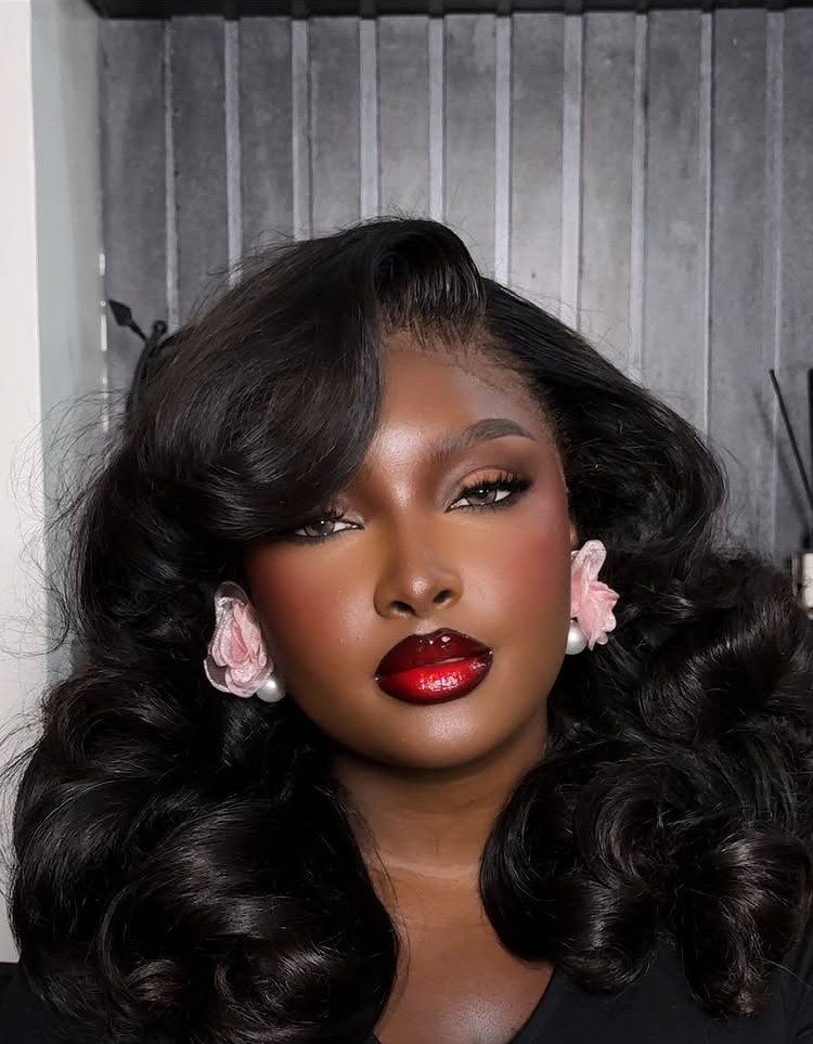 Woman with dark skin wearing deep red glossy lipstick and pink flower earrings.