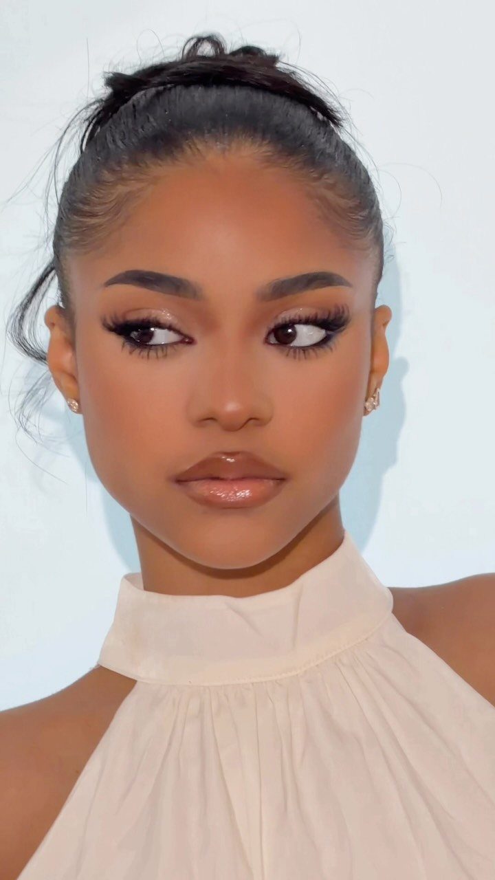Woman with dark skin wearing elegant wedding makeup and a cream high-neck top.