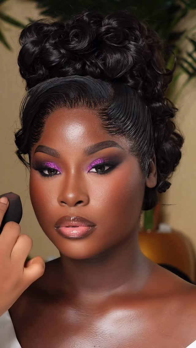 Woman with dark skin wearing purple glitter wedding makeup and a curly updo.