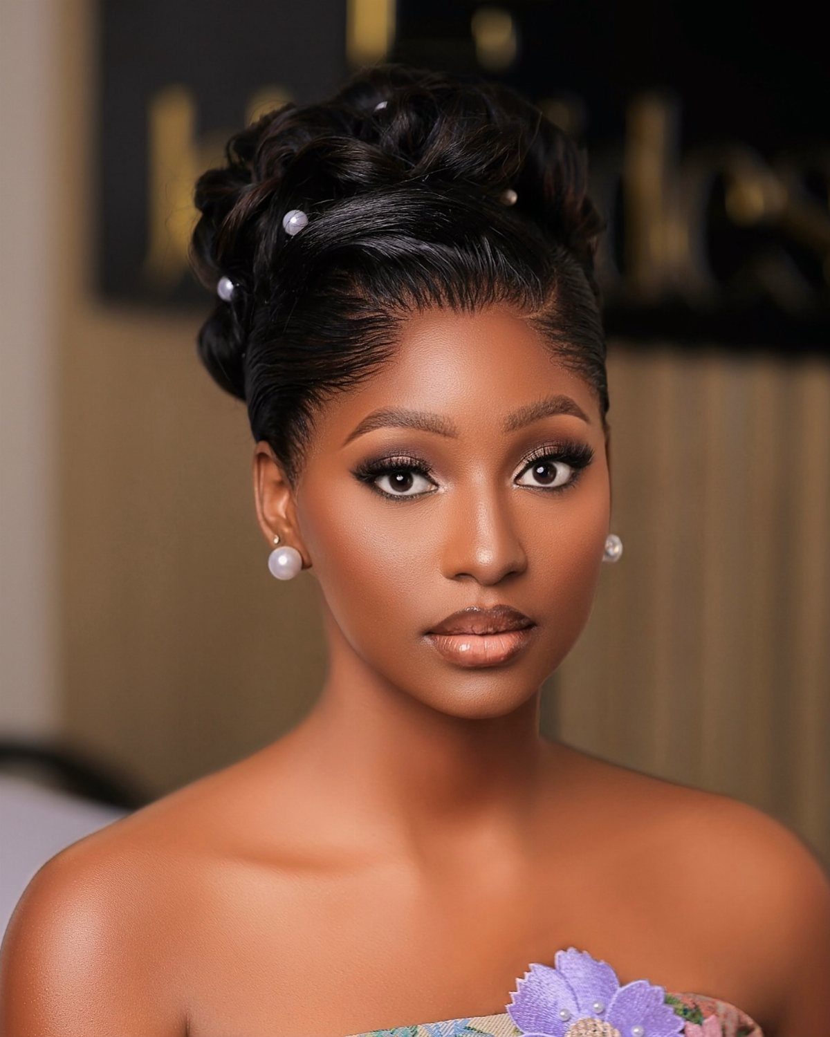 Woman with dark skin wearing glamorous wedding makeup and a pearl-accented updo.