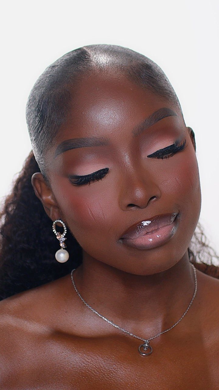 Woman with dark skin wearing warm earthy eyeshadow and glossy lip makeup.