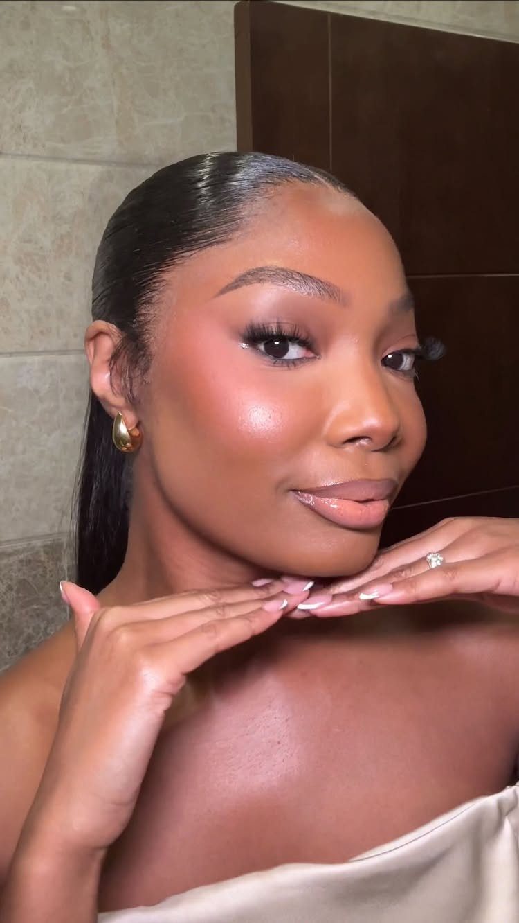 Woman with dark skin wearing soft glam makeup with glowing skin and nude lips
