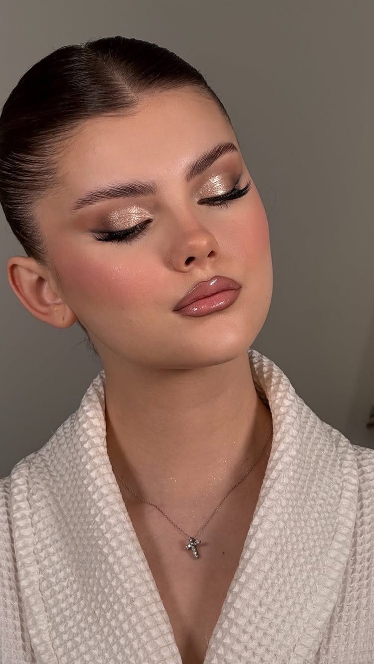 Woman with shimmering champagne eyeshadow, glossy lips, and a white textured robe.