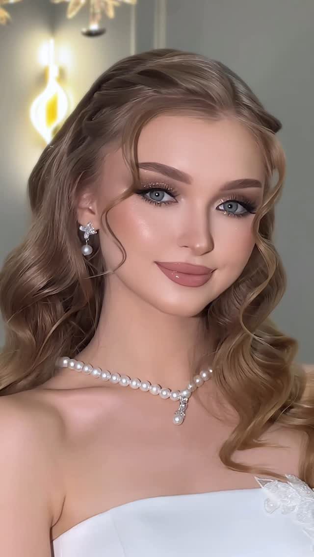Woman with blue eyes wearing classic bridal makeup, pearl necklace, and white dress.