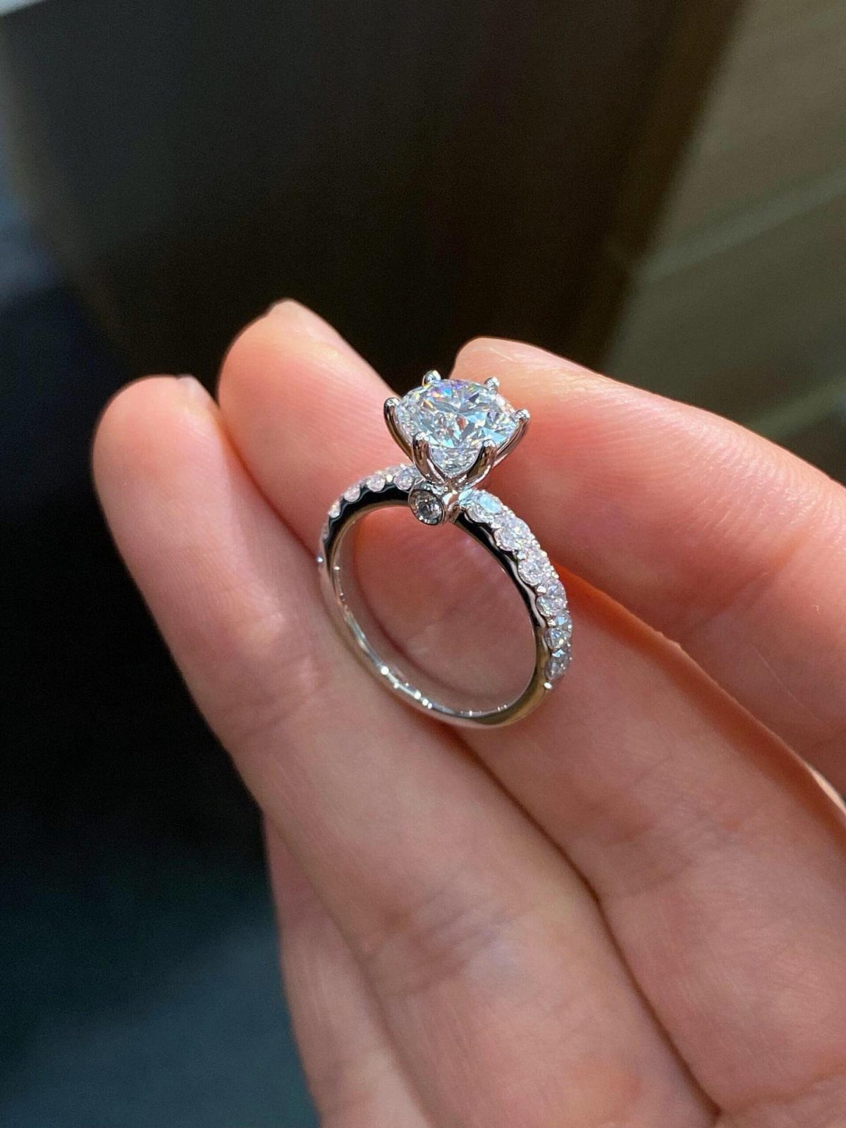 Silver diamond ring with a large center stone and pavé band held by fingers.