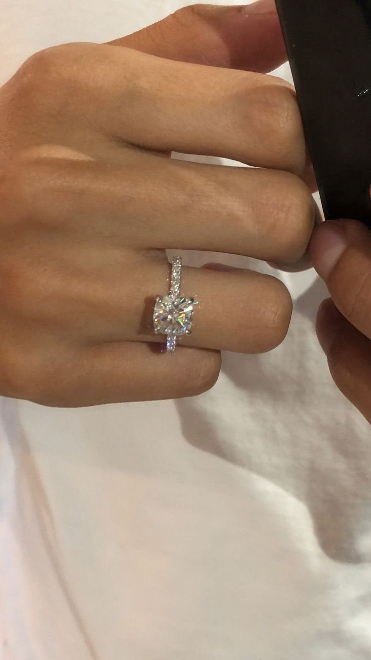 Square-cut diamond wedding ring on a person's finger against a white background
