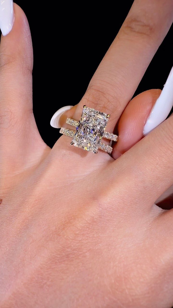 Large emerald-cut diamond ring and matching band on a finger with white nails.