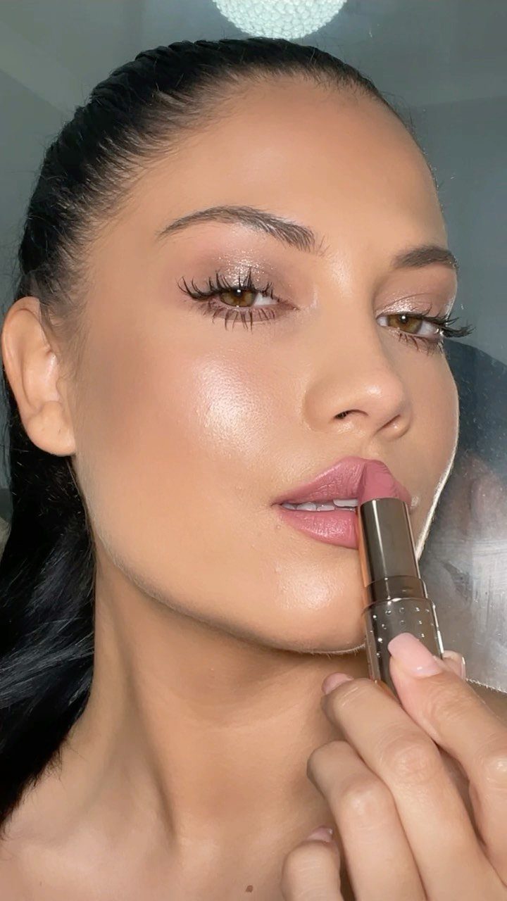 Woman with glowing skin and soft glam makeup holding a gold lipstick tube.