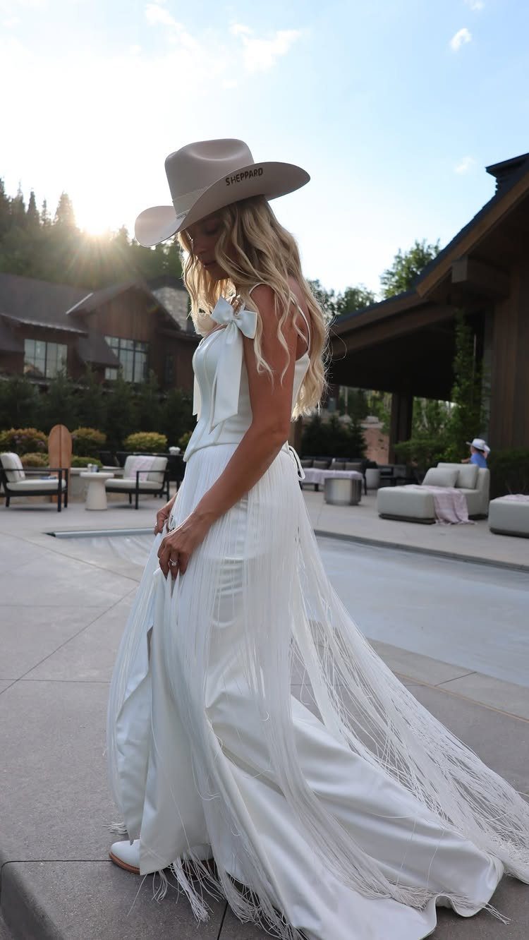 Woman in a white fringed wedding dress and tan cowboy hat on a patio
