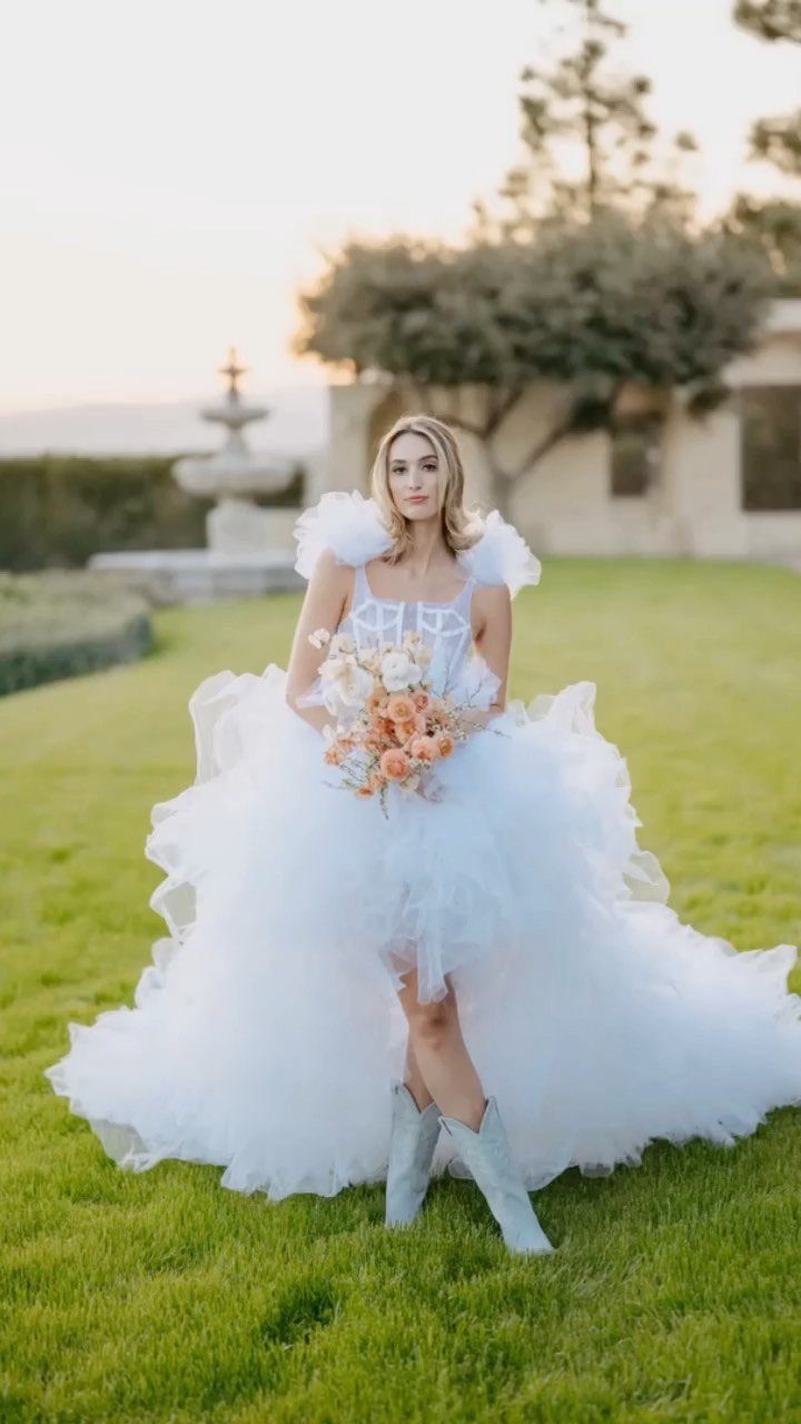 Woman in a white ruffled wedding dress and light blue cowboy boots holding flowers.