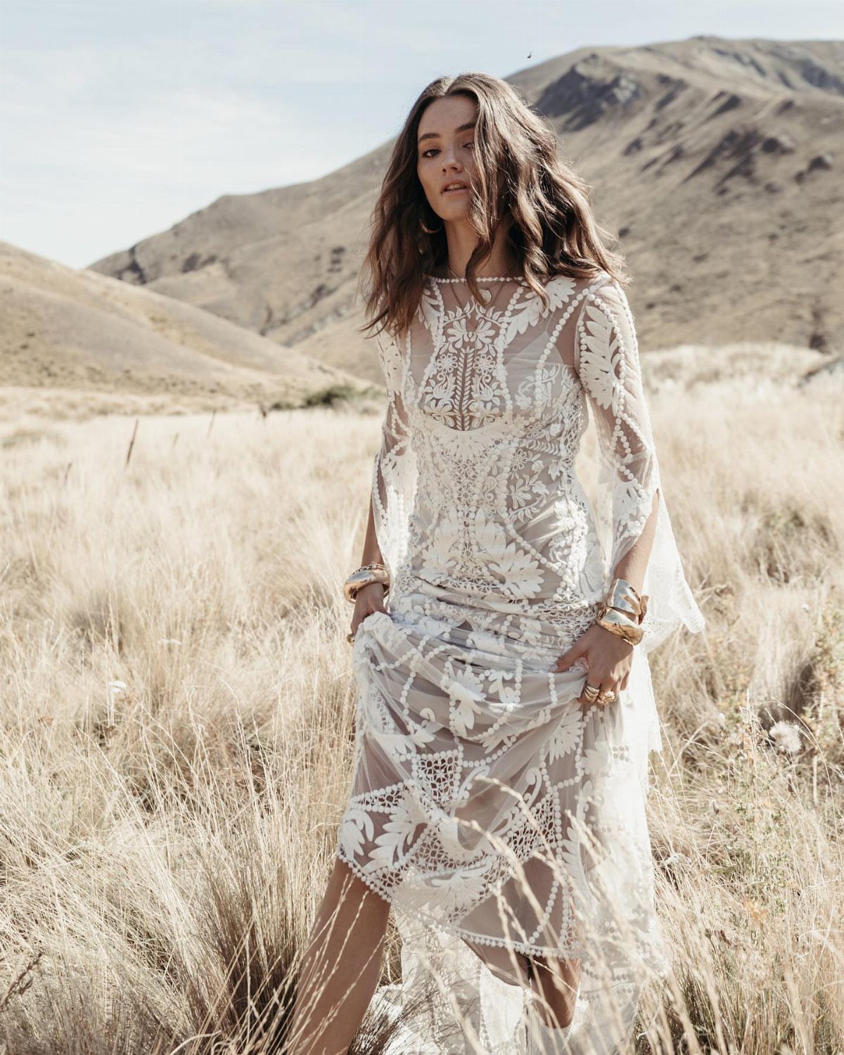 Woman in a high neckline lace wedding dress standing in a mountain field.