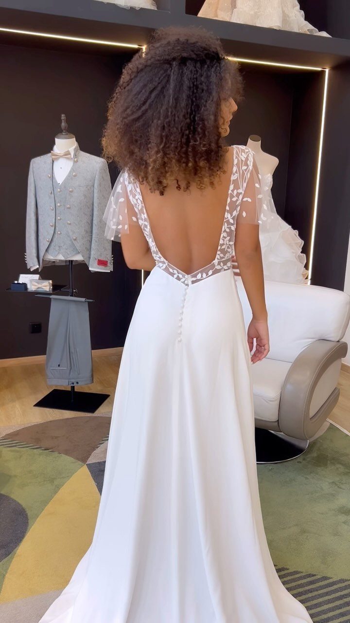 Woman wearing a white wedding dress with a deep open back and lace sleeves.