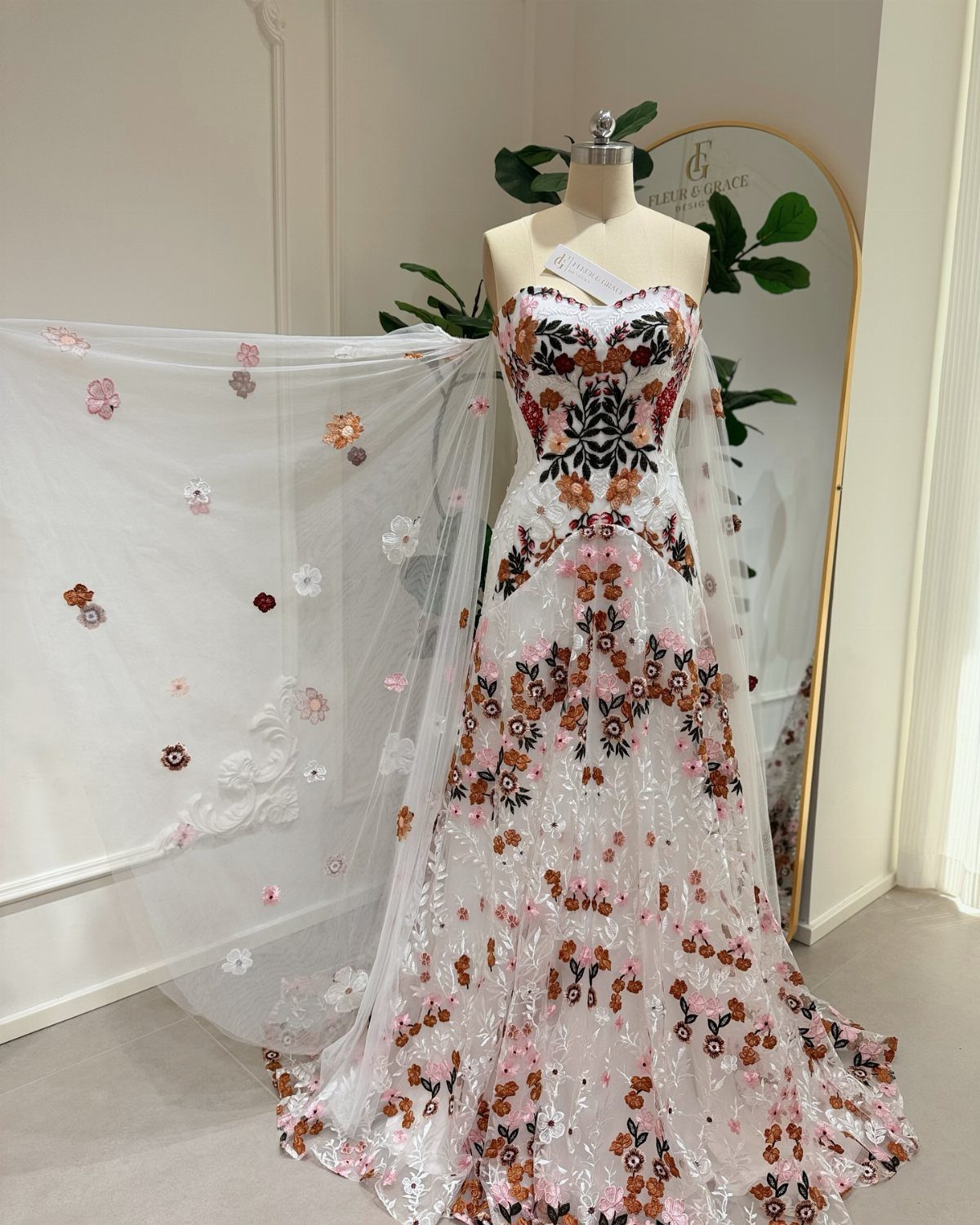 Strapless white wedding dress on a mannequin with colorful floral embroidery and matching veil.