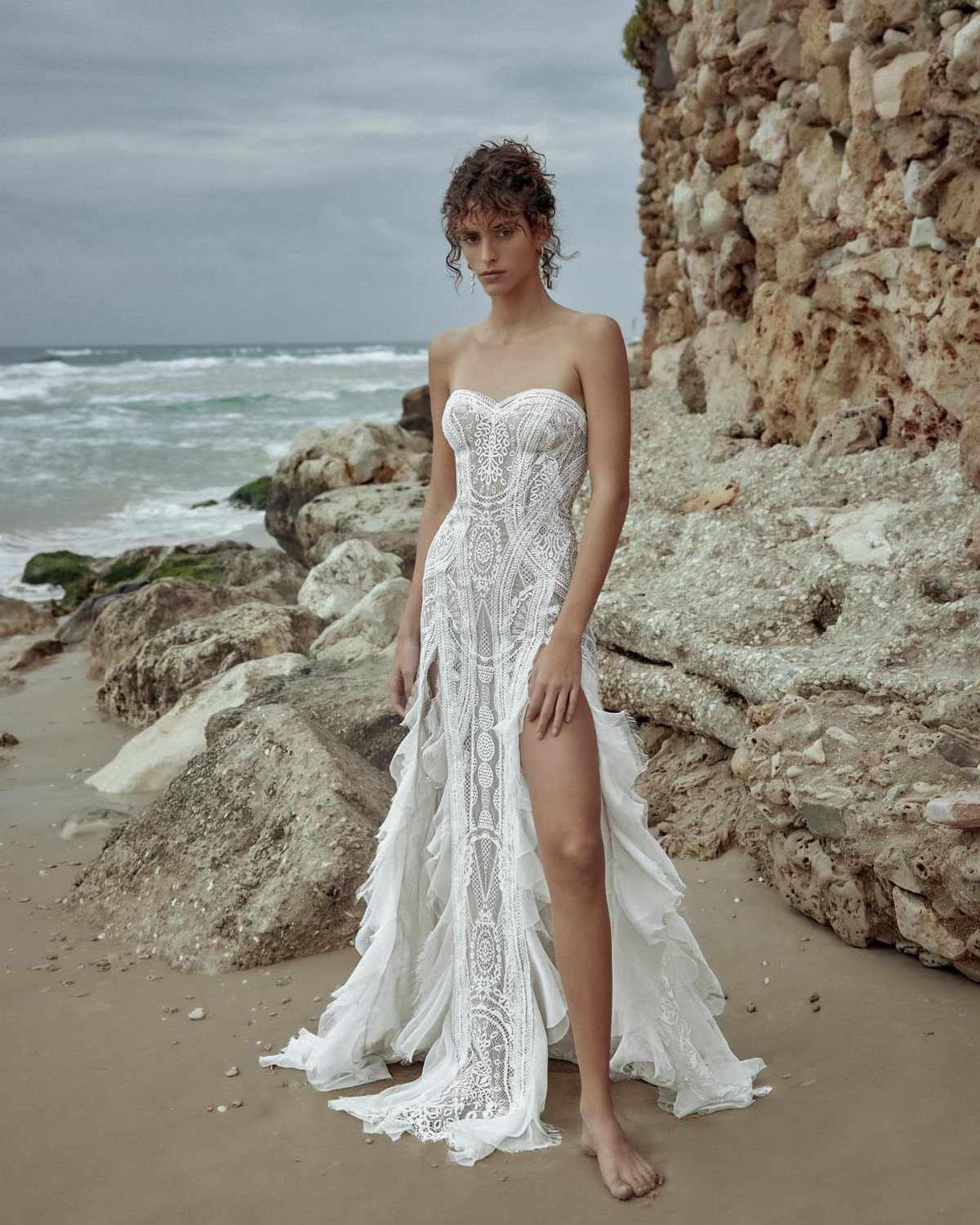 Woman in a strapless white lace wedding dress standing on a rocky beach