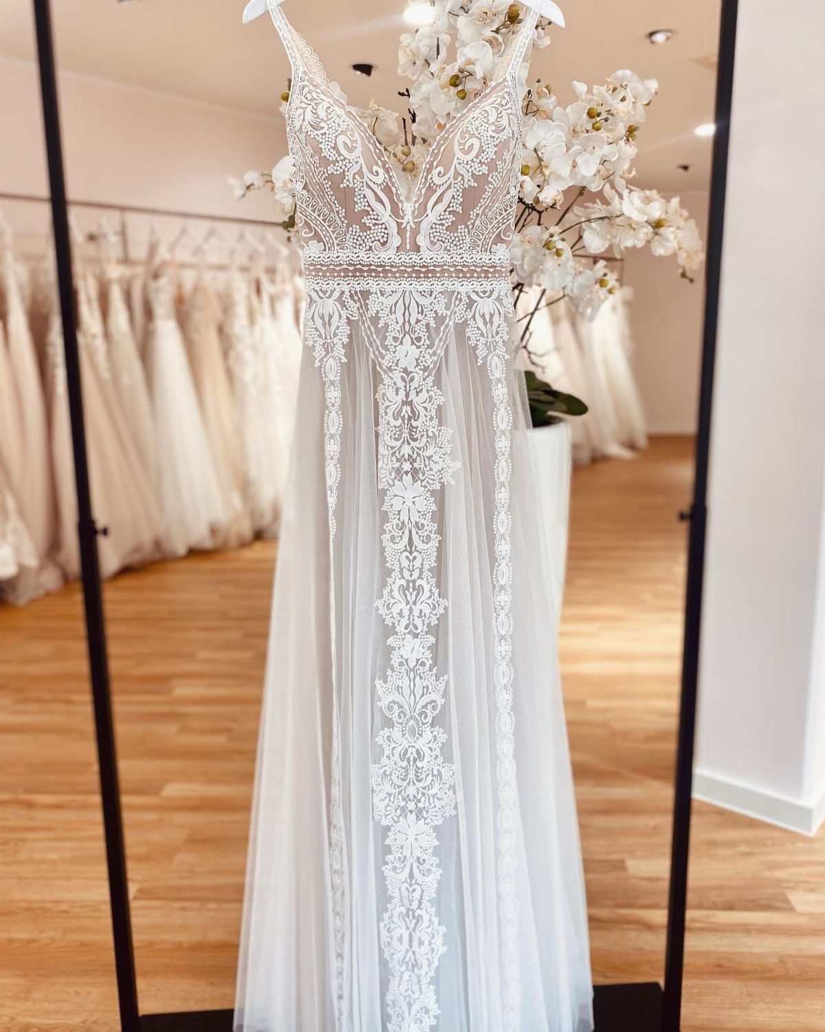 White bohemian wedding dress with intricate lace embroidery displayed in a bridal boutique.